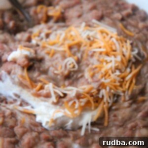 refried beans with sour cream, a spoon, and cheese in a small bowl up close.