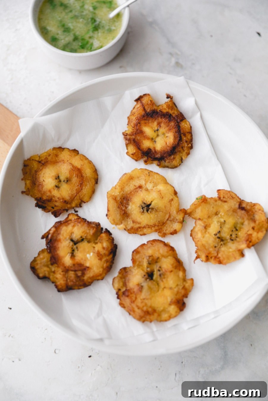 6 tostones on a white plate with a side of garlic butter sauce. 