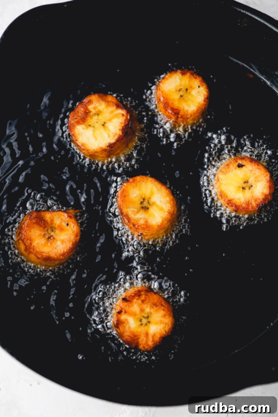 6 plantains frying in a cast iron skillet. 