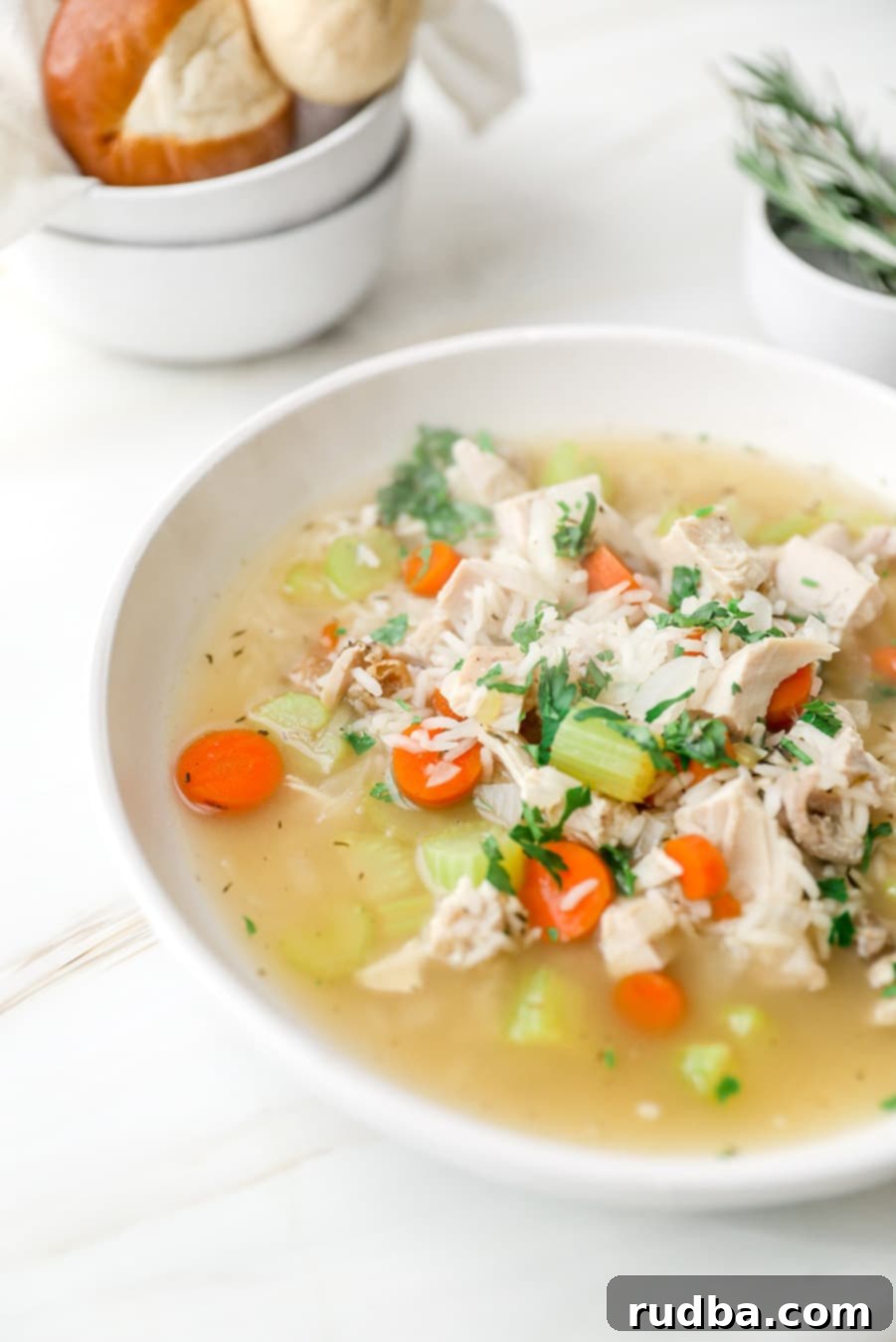 Close-up of a warm bowl of turkey and rice soup, with crusty bread in a smaller bowl in the background.