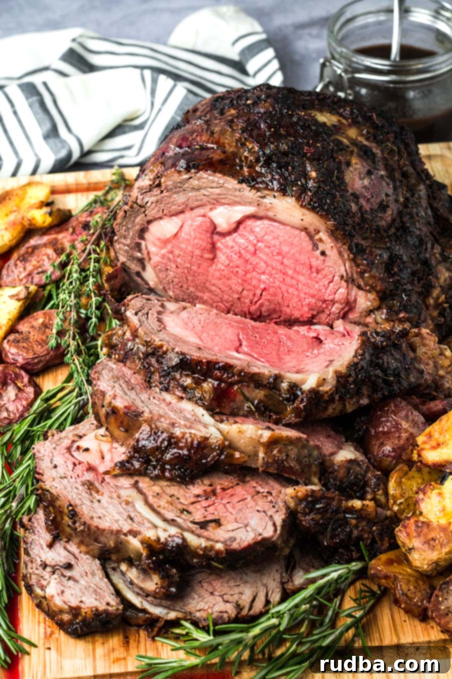 sliced prime rib medium rare on a wooden board with fresh rosemary and thyme.