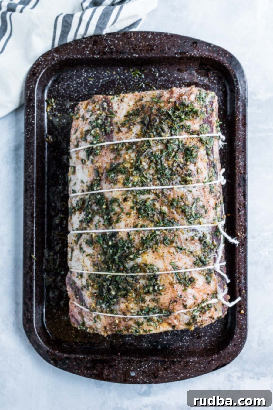 an entire raw prime rib tied with kitchen twine on a baking sheet.