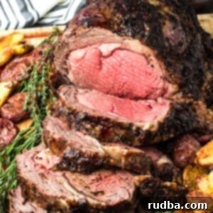Juicy Prime Rib with Rich Au Jus 8 sliced prime rib medium rare on a wooden board with fresh rosemary and thyme.