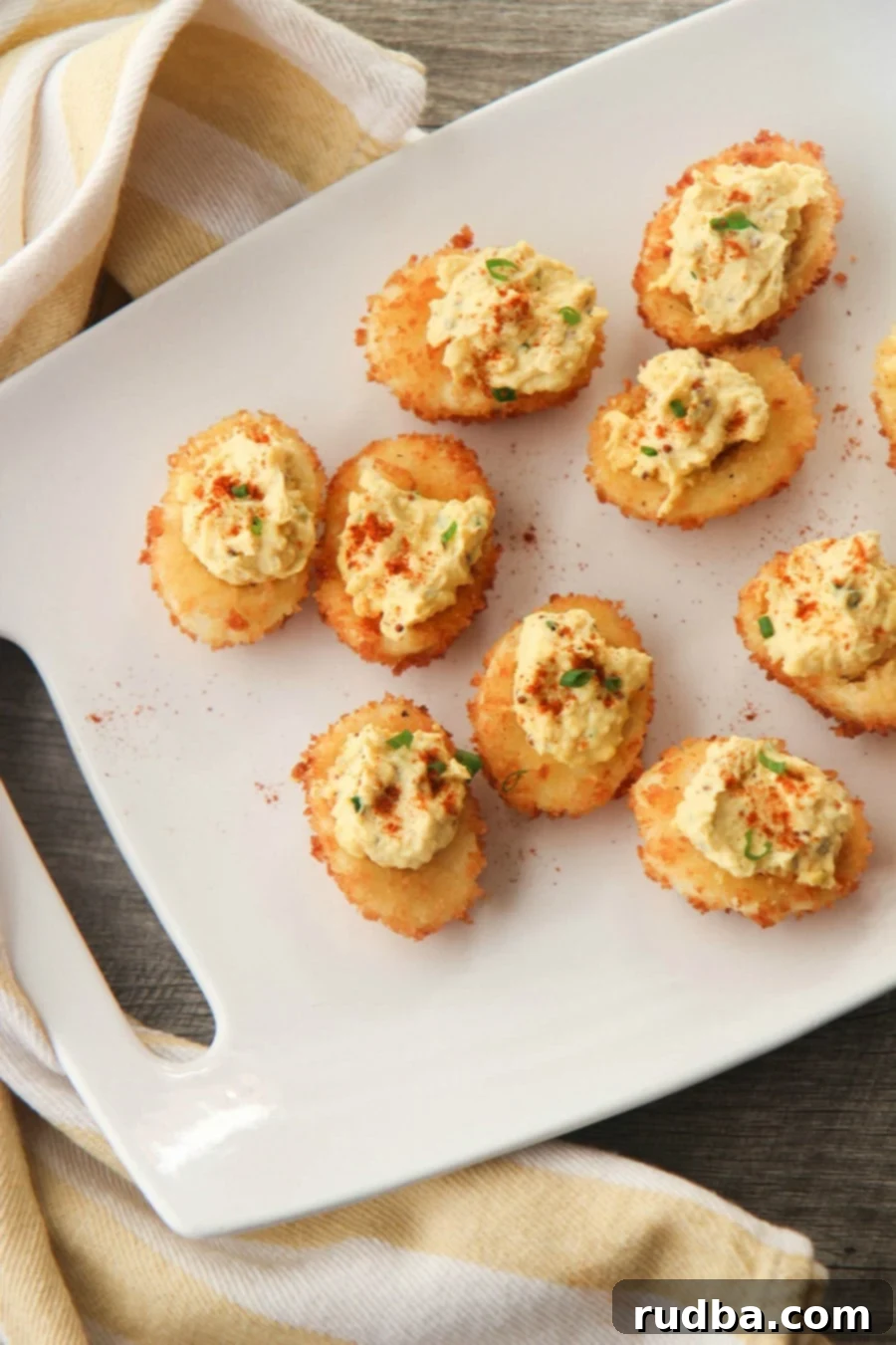 nine fried deviled eggs on a white platter with a yellow and white towel on the side. 
