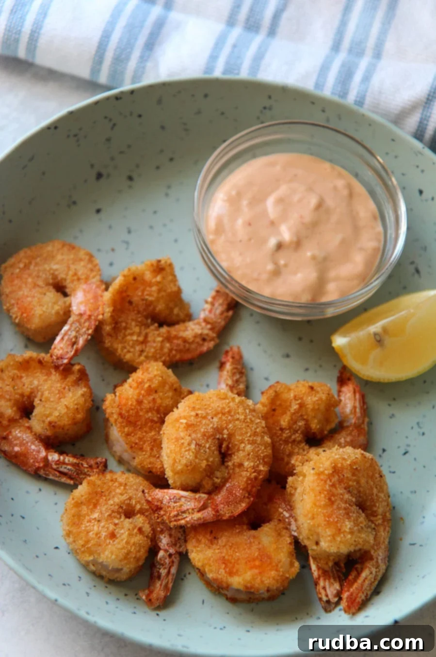 air fried shrimp on a blue plate with a lemon wedge and sauce in a bowl.