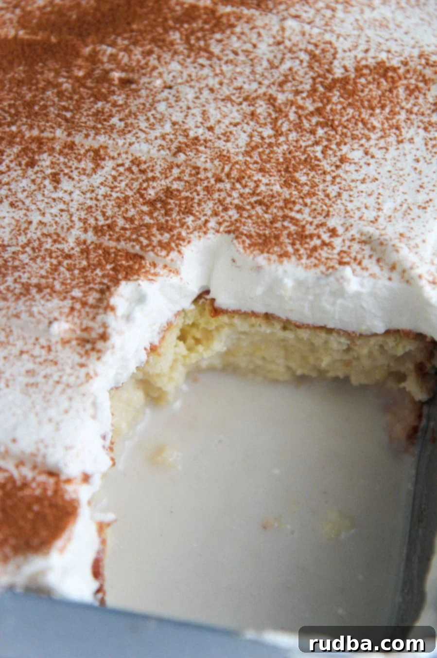 A whole Coquito cake in a glass baking dish, with one slice already removed, showing the moist interior.