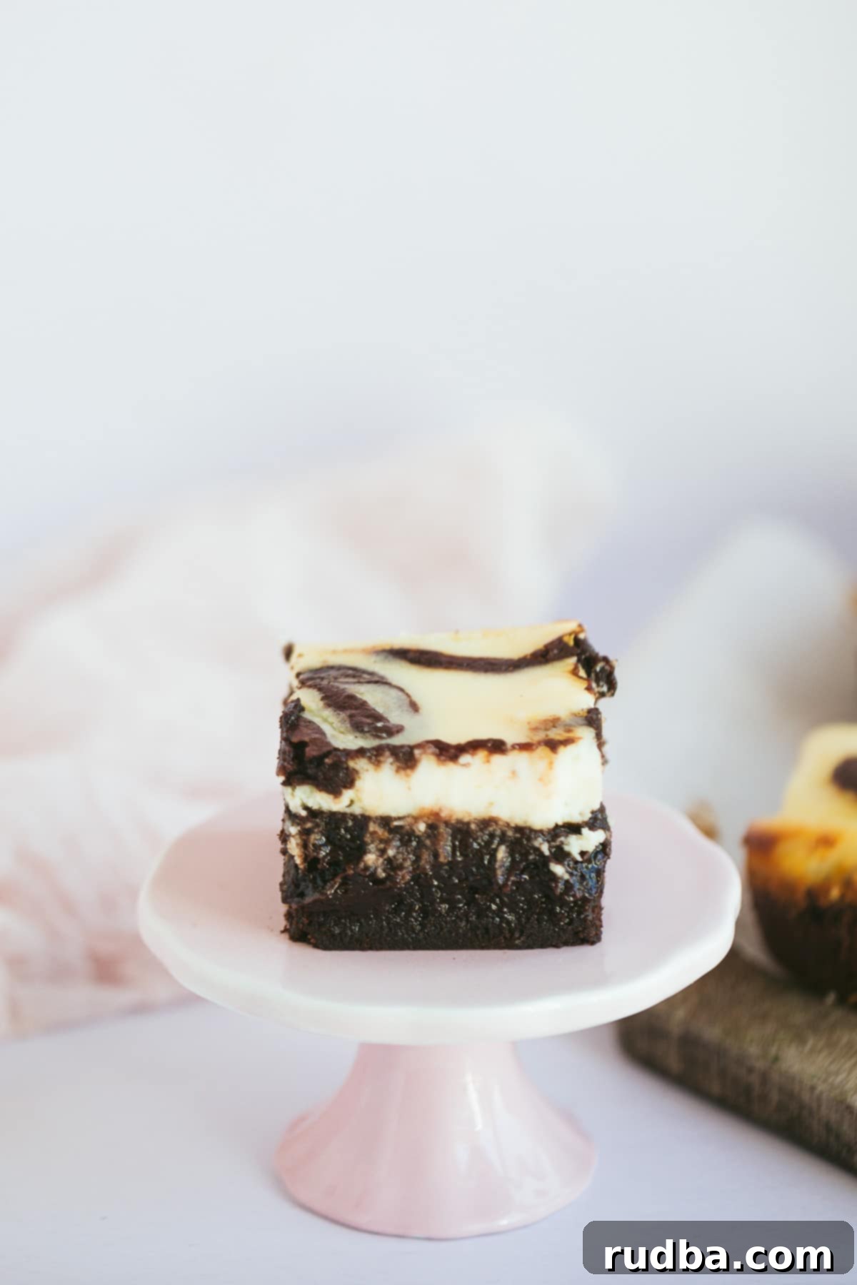 A squared cheesecake brownie slice on a pink cake stand, showcasing the beautiful swirl.