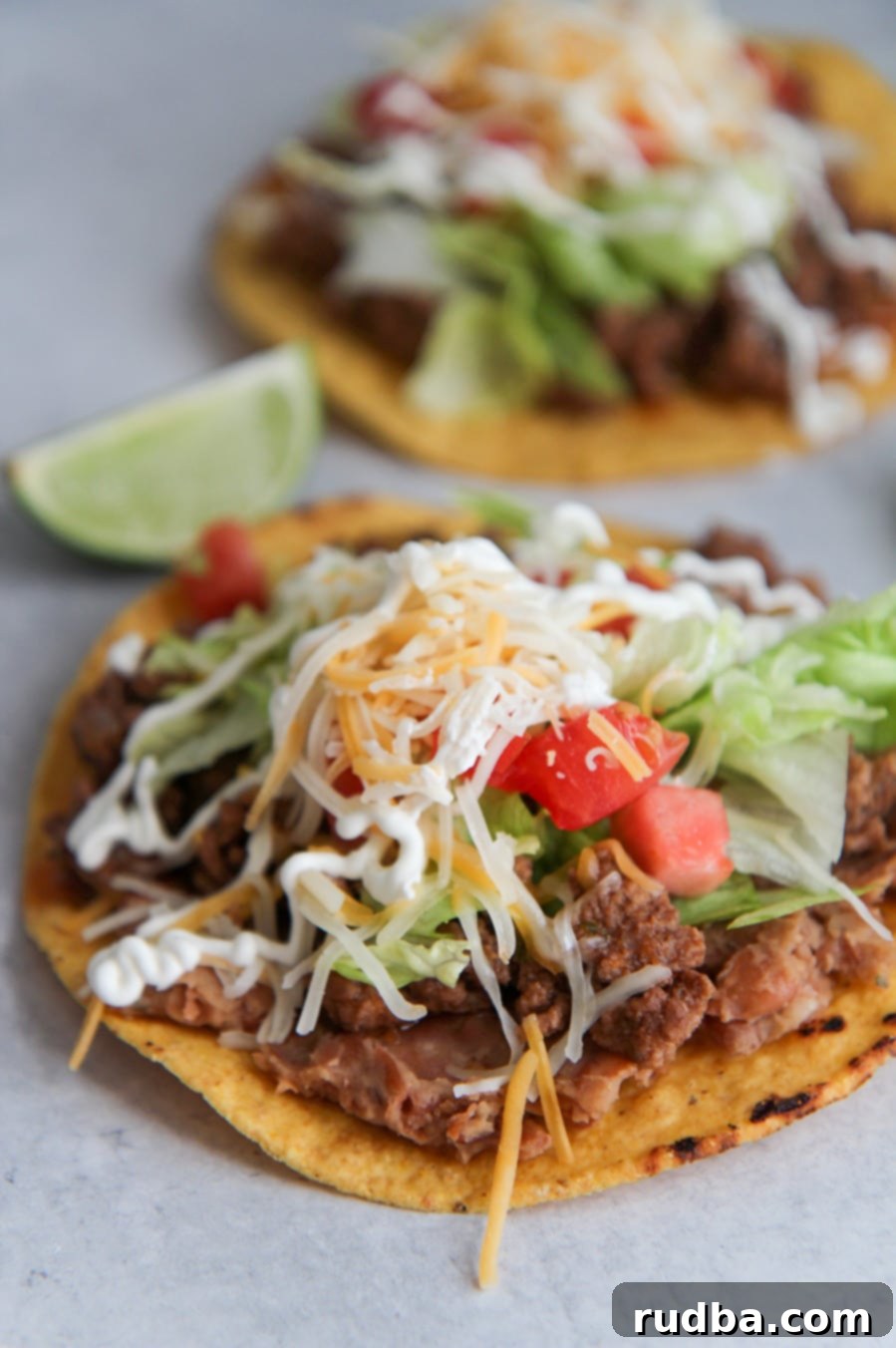 two beef tostadas with refried beans, lettuce, tomatoes, cheese, sour cream, and limes on the side. 