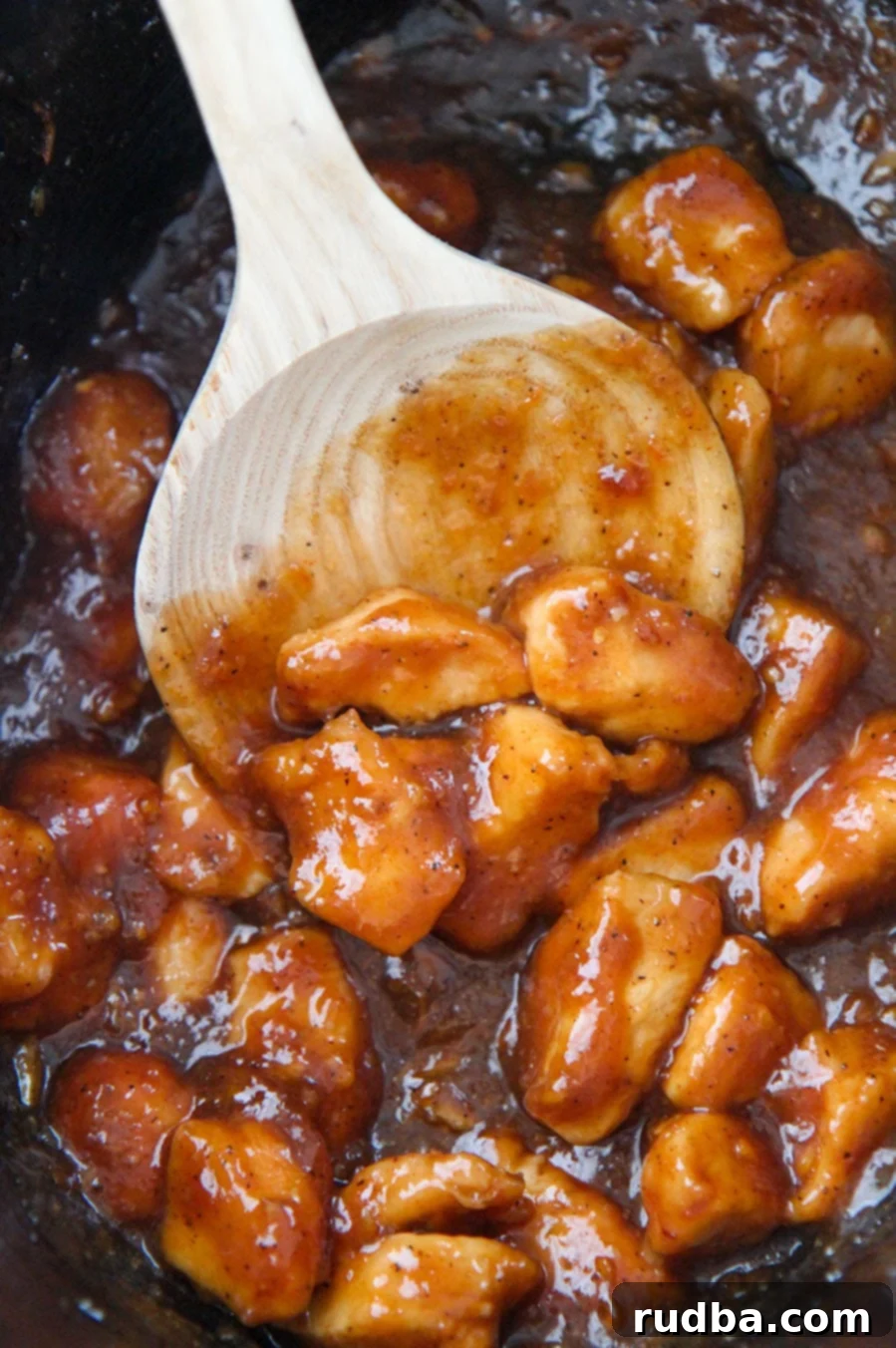 Orange chicken cooking in a slow cooker, with a wooden spoon stirring the rich, glossy sauce and tender chicken pieces.