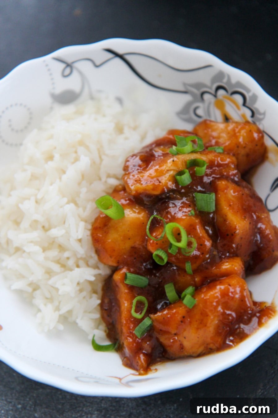 Close-up of crockpot orange chicken garnished with fresh scallions, served alongside a portion of fluffy white rice.
