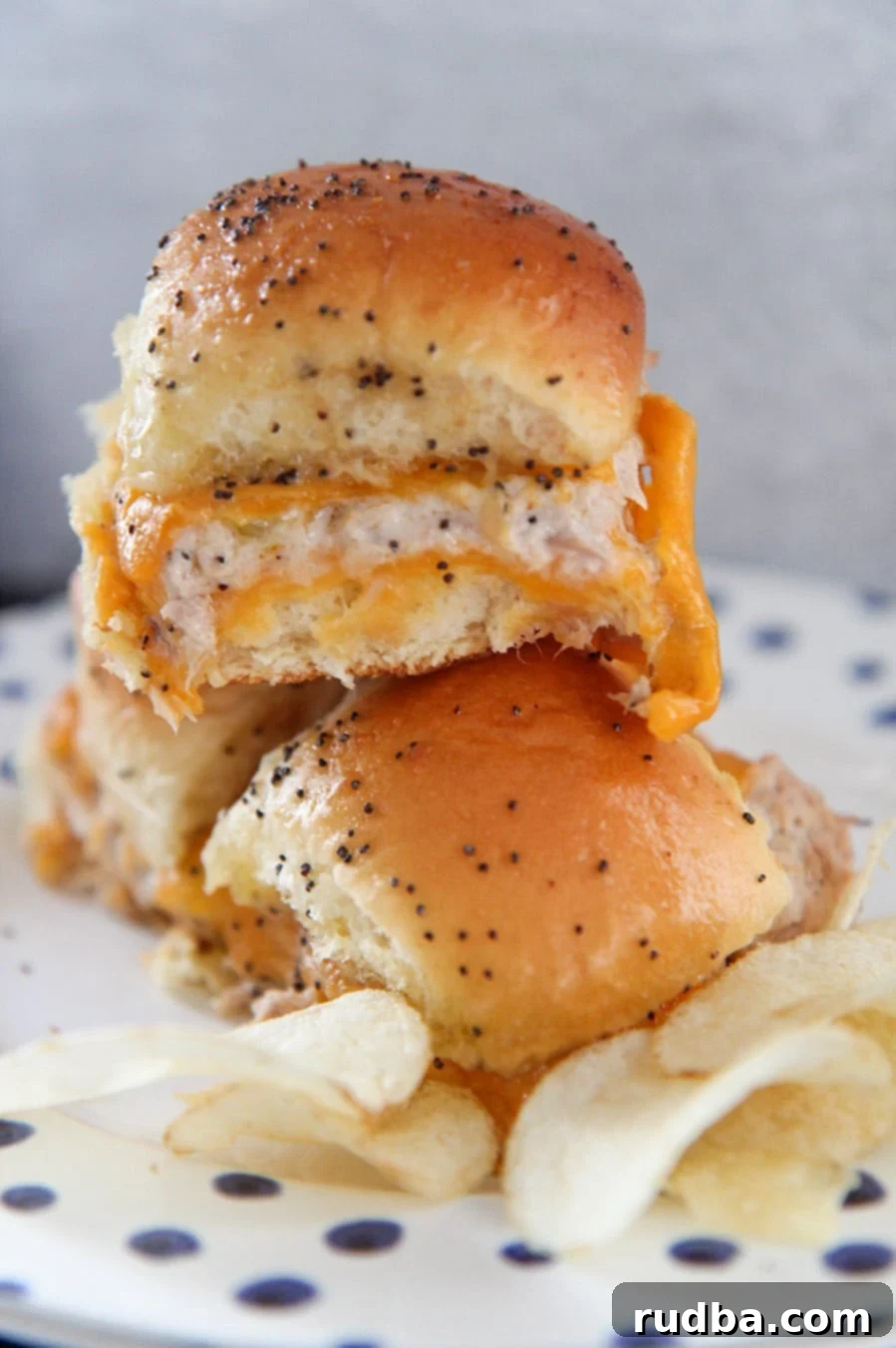 Three hot tuna melt sliders with potato chips on a white plate, showcasing their golden-brown tops and melted cheese.