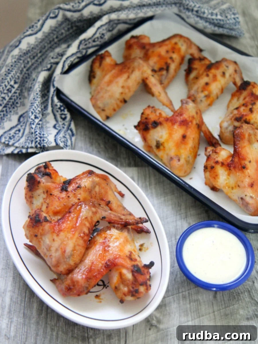 oven roasted chicken wings on a small white plate with a side of blue cheese dip and more chicken wings in the background.