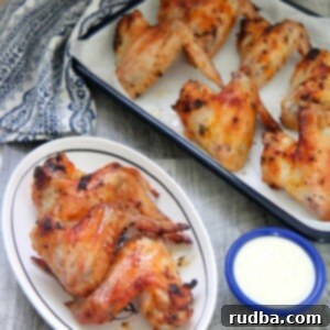 Crispy Oven Roasted Chicken Wings 5 oven roasted chicken wings on a small white plate with a side of blue cheese dip and more chicken wings in the background.