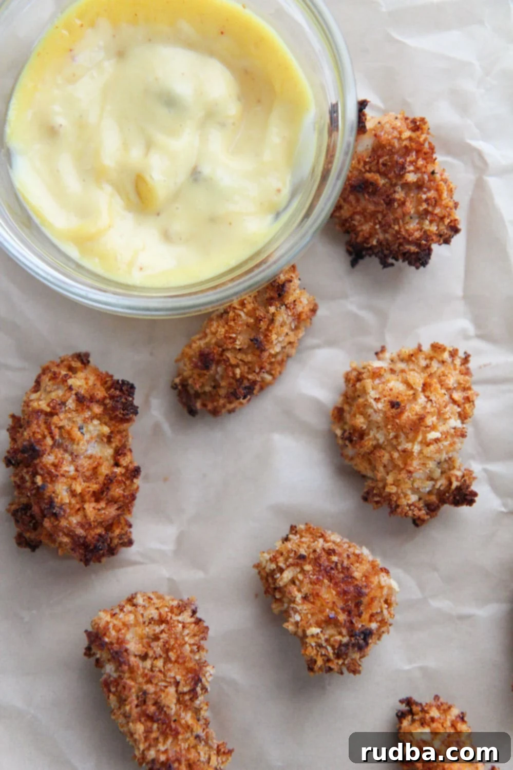 baked spicy popcorn chicken bites on brown parchment paper with a side of honey mustard.