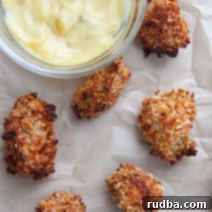 baked spicy popcorn chicken bites on brown parchment paper with a side of honey mustard.