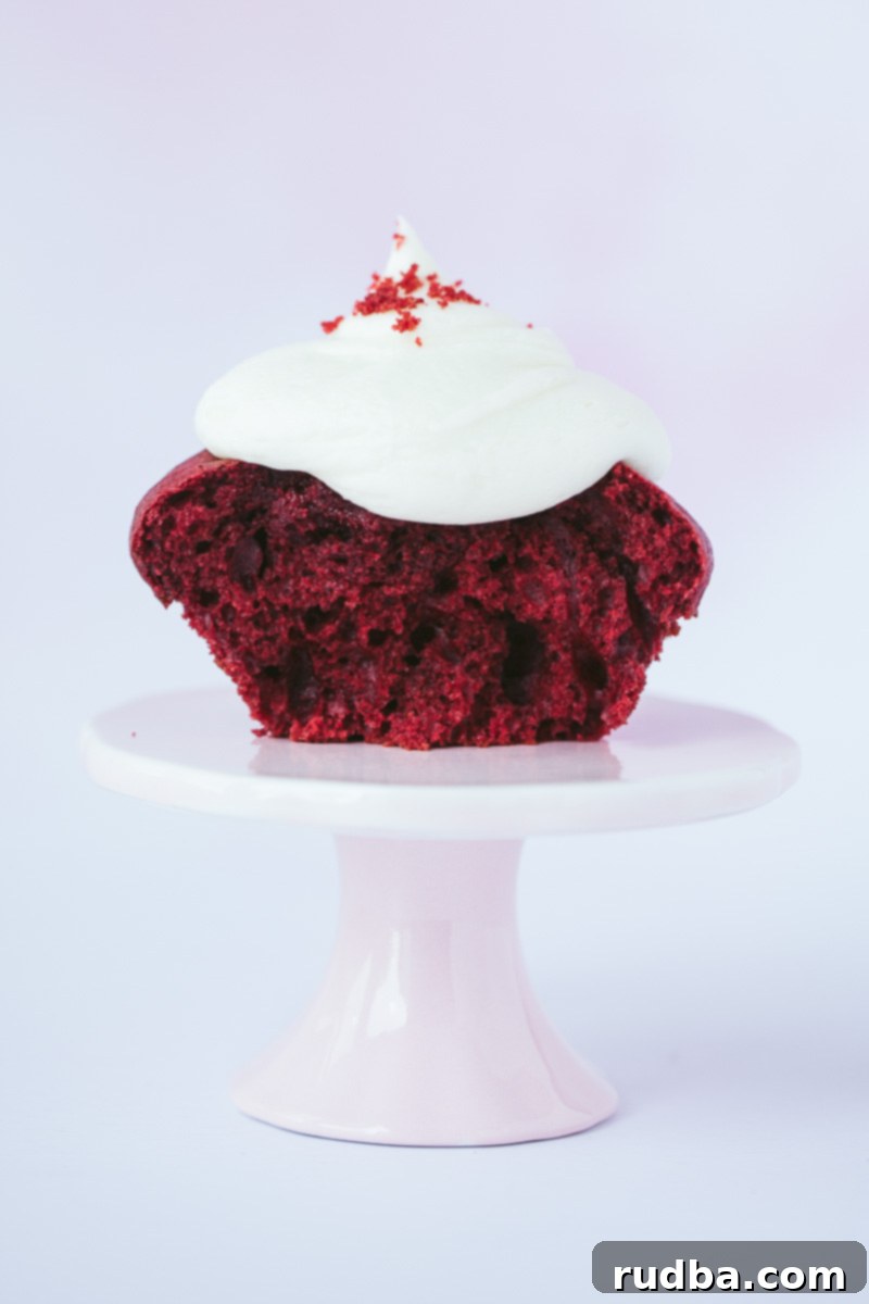one red velvet cupcake with cream cheese frosting sliced in half on top of a pink cake stand. 