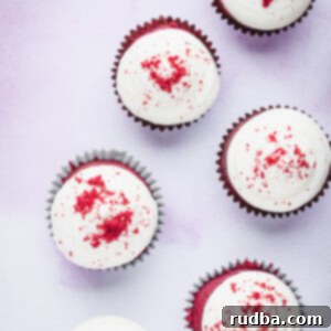 Six red velvet cupcakes with cream cheese frosting and cupcake crumbs on top.