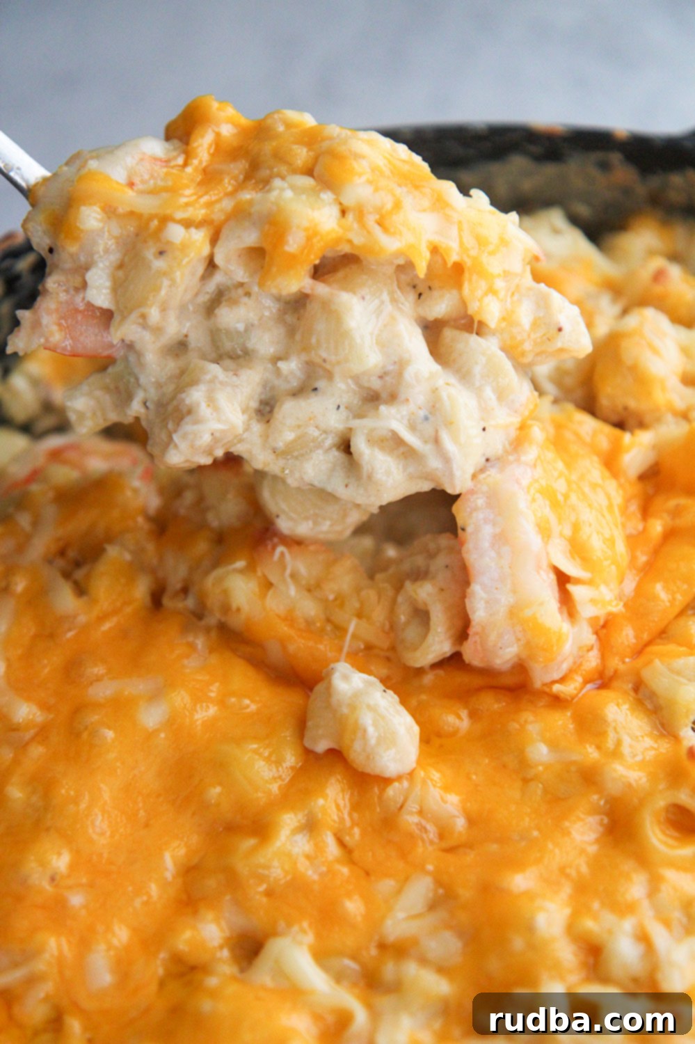 A close-up of a spoonful of creamy seafood mac and cheese, showing pieces of shrimp and crab, lifted from a skillet.