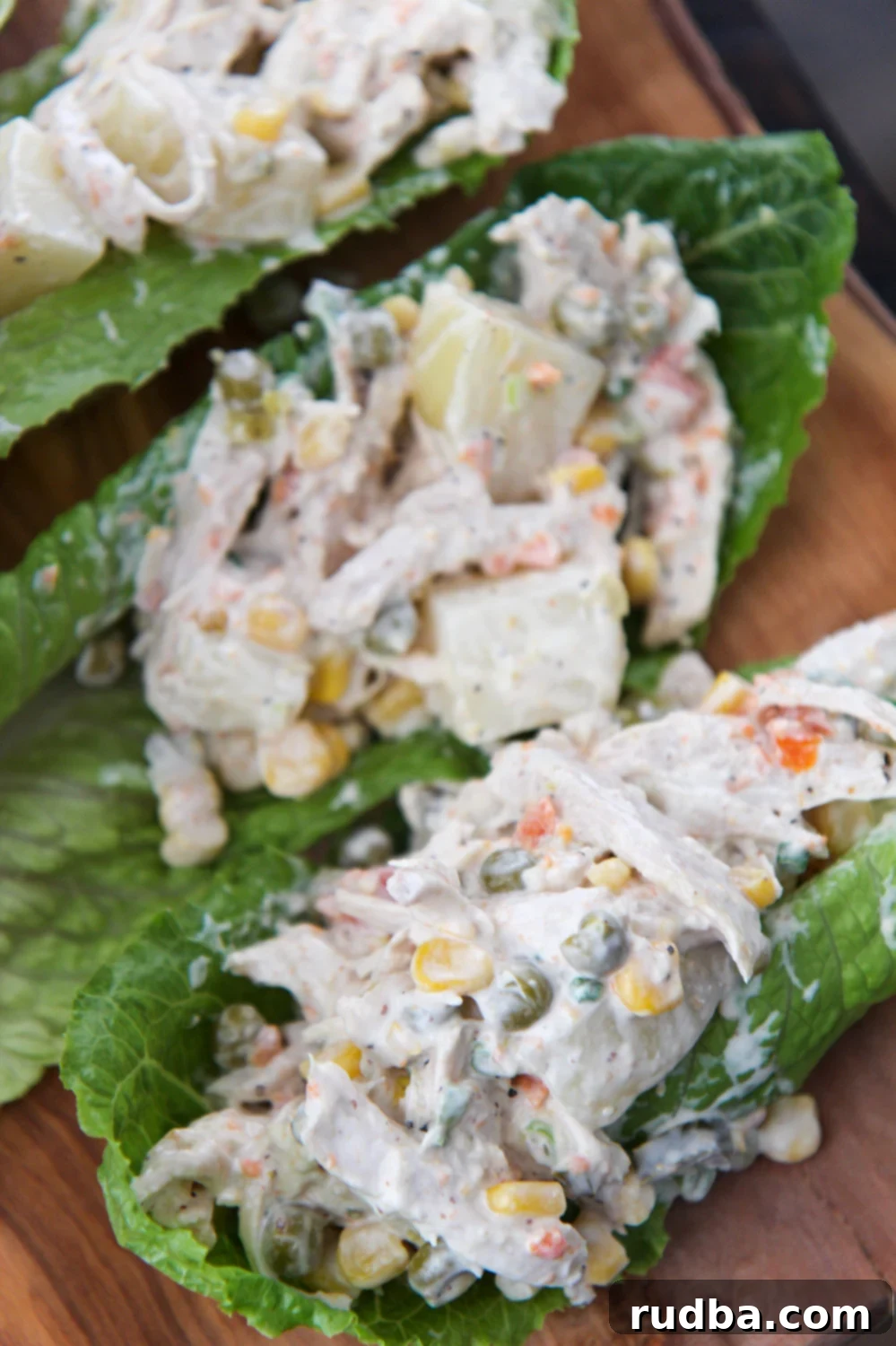 ensalada de pollo (chicken salad) on three lettuce cups. A close-up shot of the creamy Mexican chicken salad served in vibrant green lettuce cups, garnished with fresh cilantro and a lime wedge. The salad is rich with shredded chicken, diced potatoes, corn, peas, and carrots.