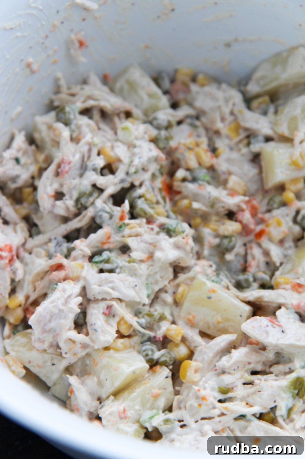 Mexican chicken salad in a white bowl. A vibrant bowl of creamy Mexican chicken salad, garnished with fresh cilantro, a lime wedge, and a sprinkle of chili powder. The colors of the corn, peas, and carrots stand out against the rich, white dressing.