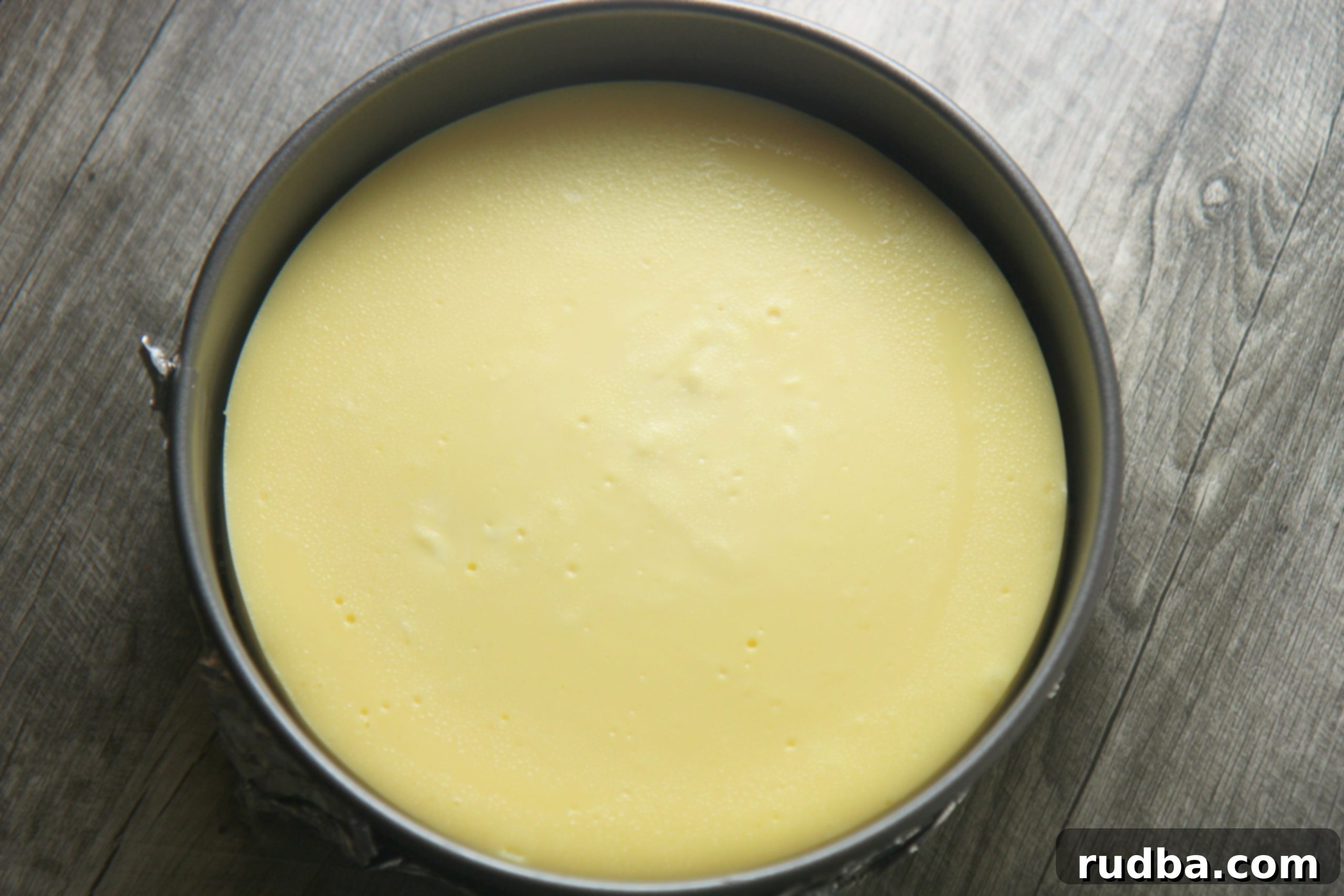 A plain, perfectly baked cheesecake resting in a springform pan, showcasing its smooth top.
