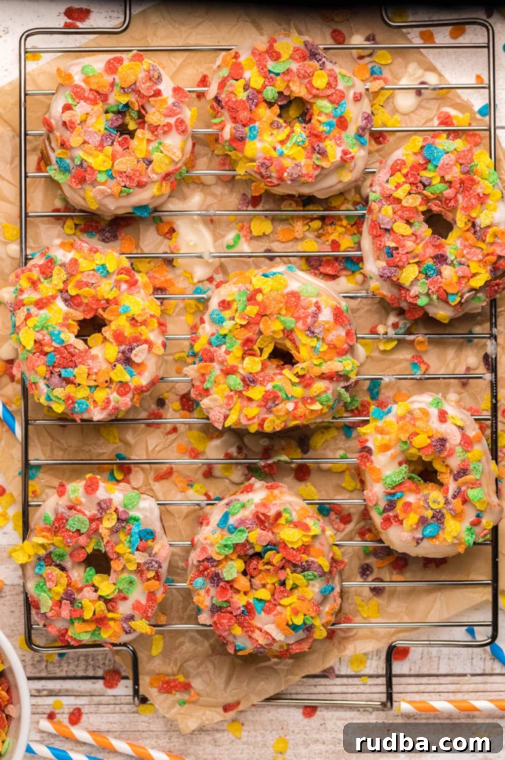 Eight colorful fruity pebble donuts arranged neatly on a wire cooling rack, showcasing their vibrant cereal topping and inviting glaze. The background is softly blurred, keeping the focus on the delicious treats.