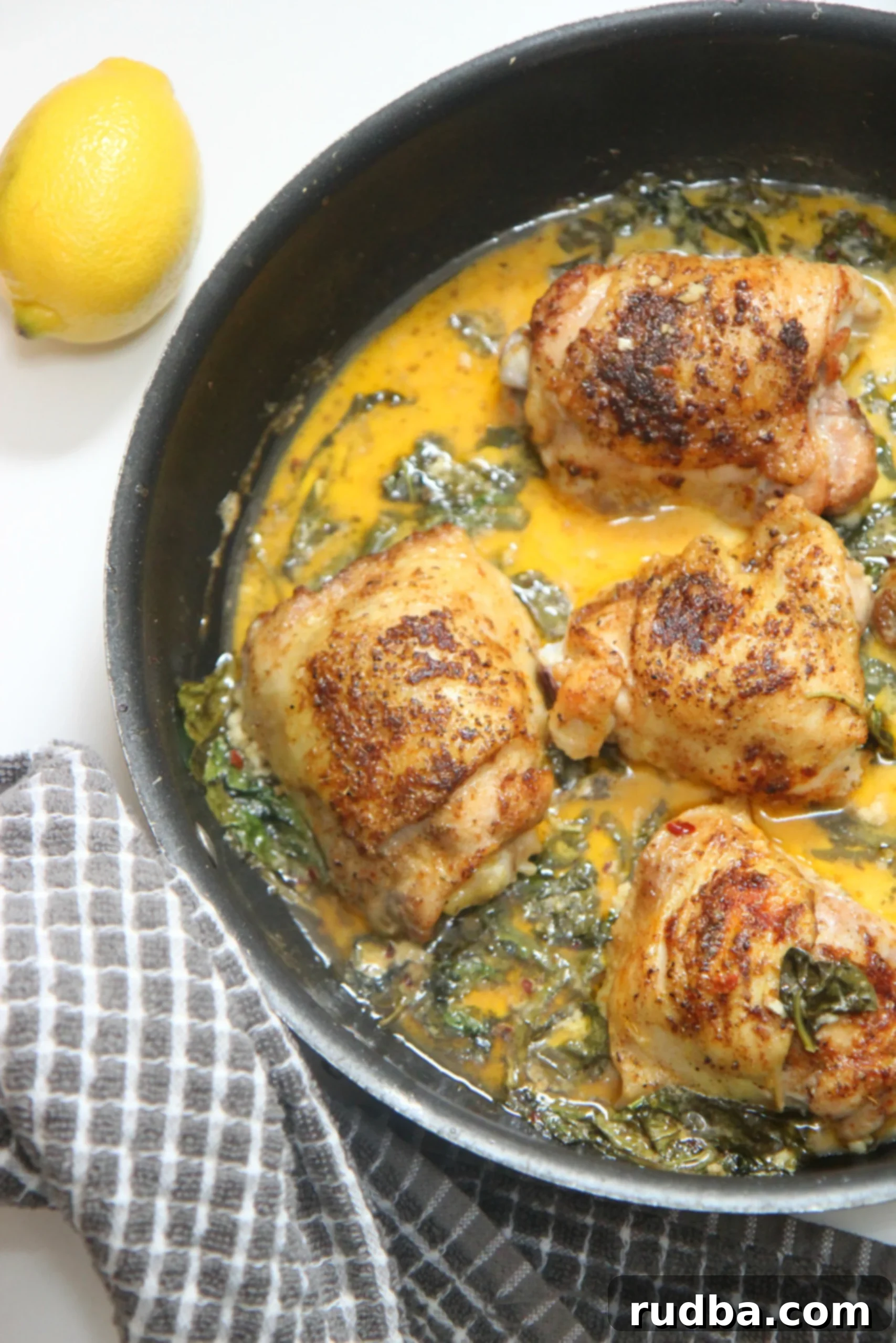 Lemon spinach chicken cooking in a black skillet with fresh lemon slices and herbs, a perfect weeknight meal.