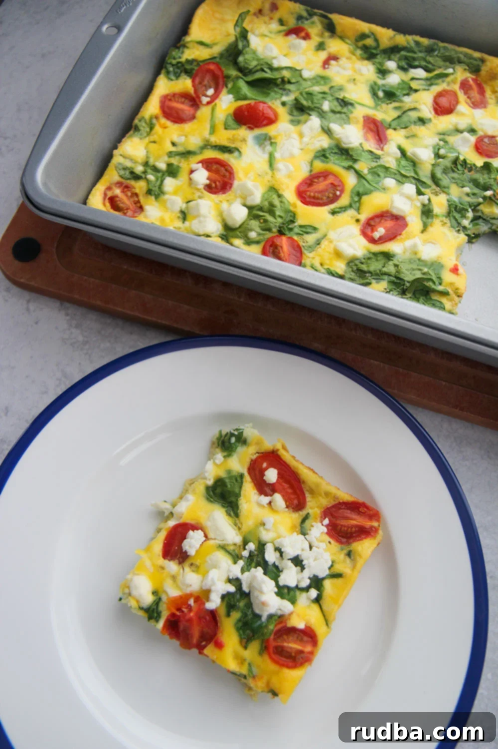 a slice of spinach and goat cheese frittata on a white and blue plate with a 9x13 frittata in the background.