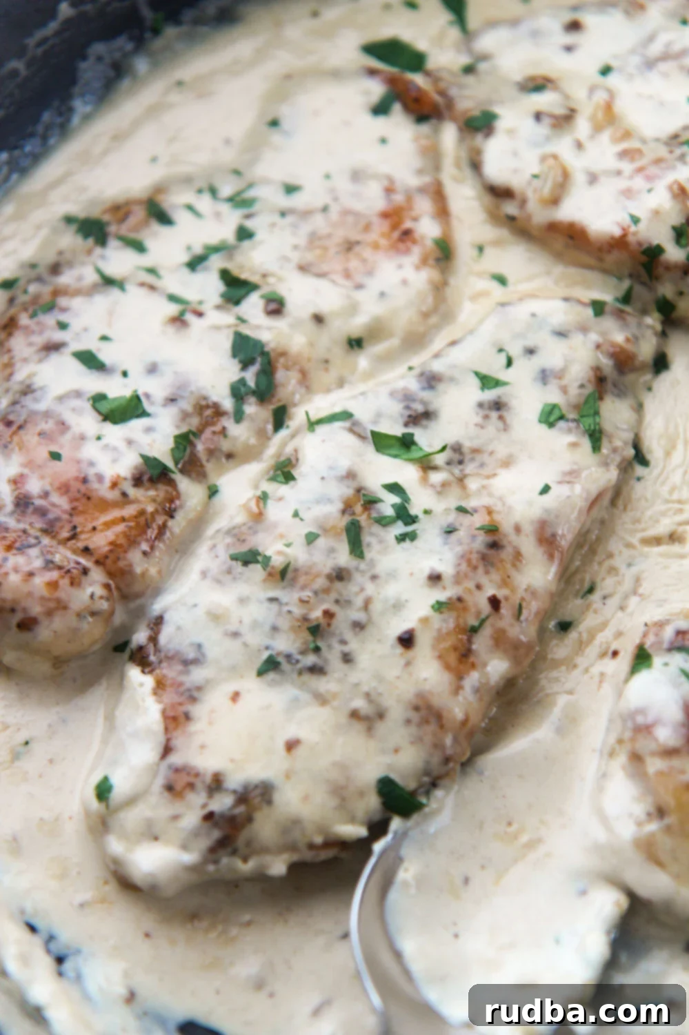Two creamy garlic parmesan chicken breasts with fresh parsley on top, served in a skillet.