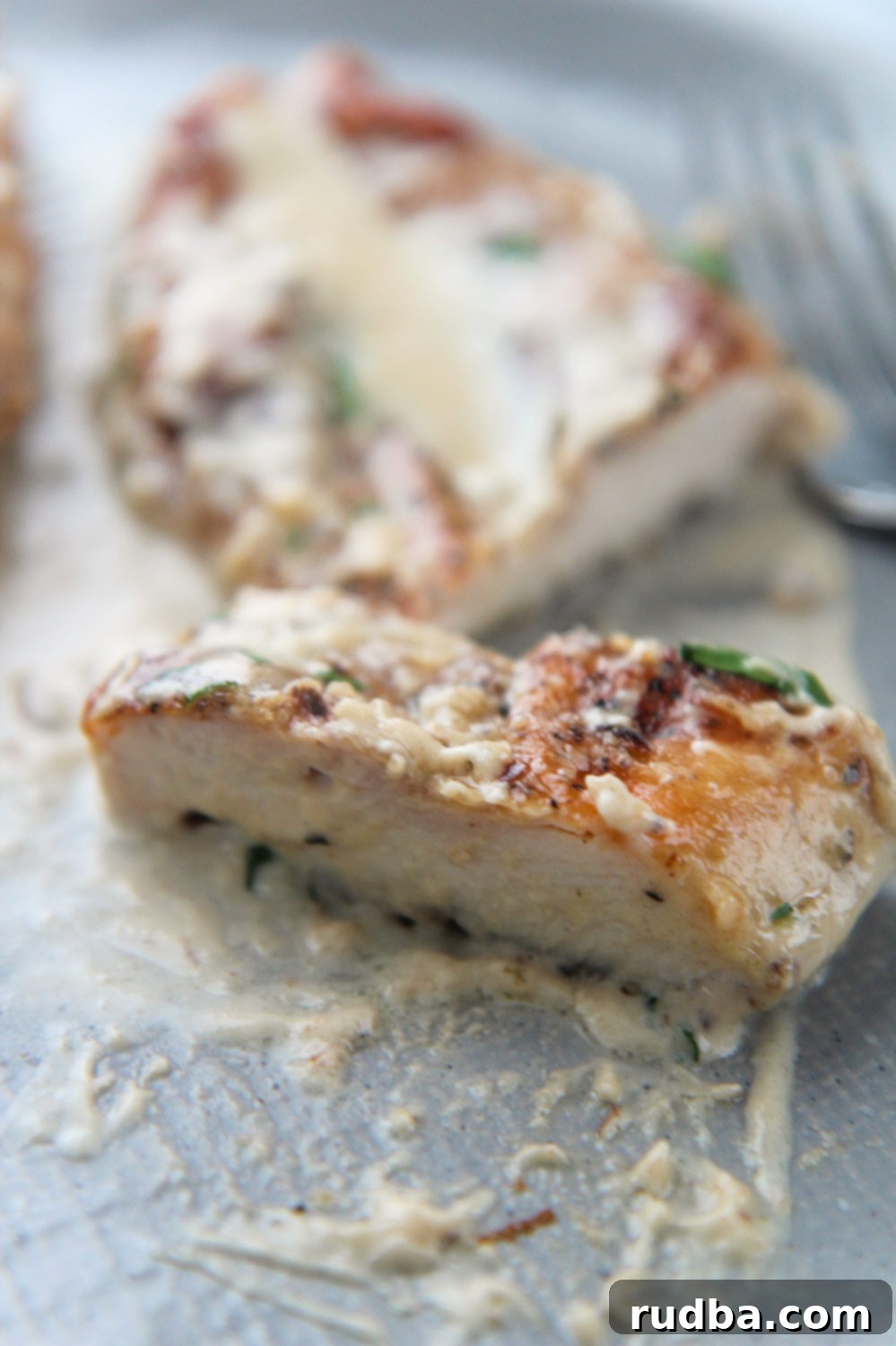 A perfectly cooked slice of creamy garlic parmesan chicken served on a gray plate, ready to eat.