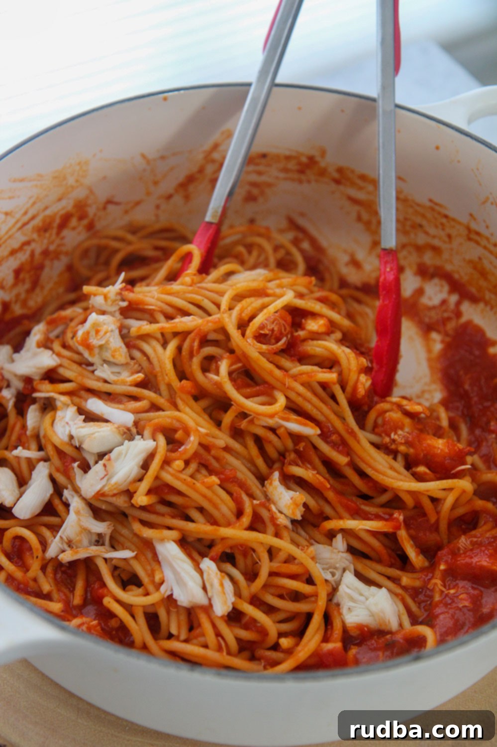 spicy crab bucatini in a white pot with red tongs.