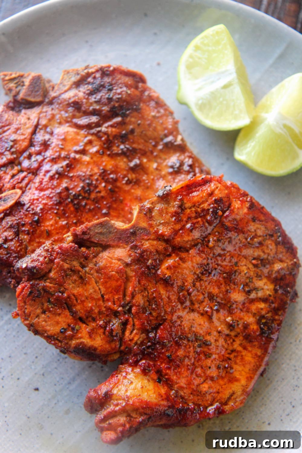Two chuletas fritas on a gray plate with two lime wedges, ready to be served.