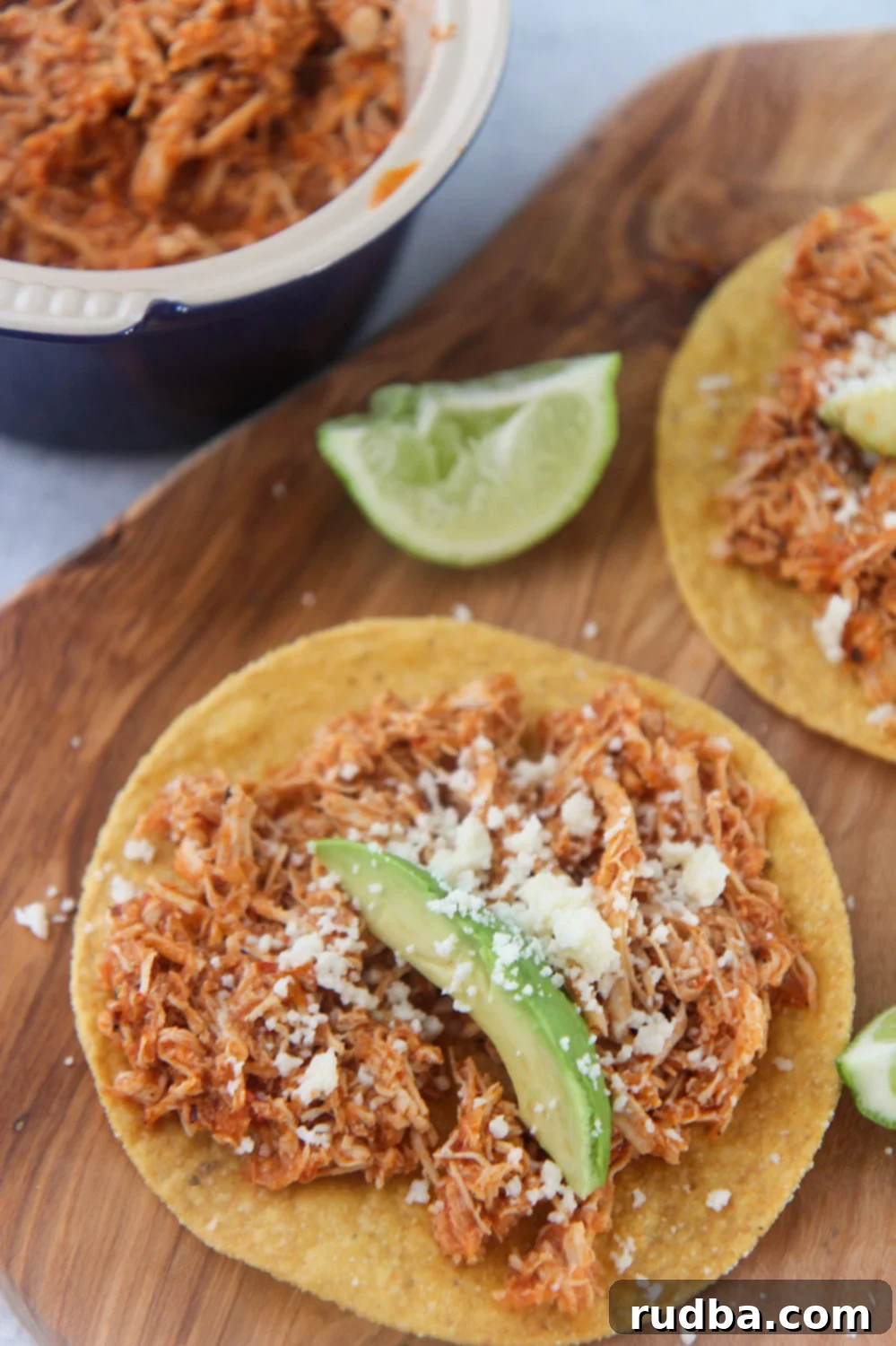 chicken tinga tostadas on a wooden board with lime wedges on the side. 