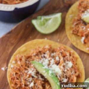 chicken tinga tostadas on a wooden board with lime wedges on the side.
