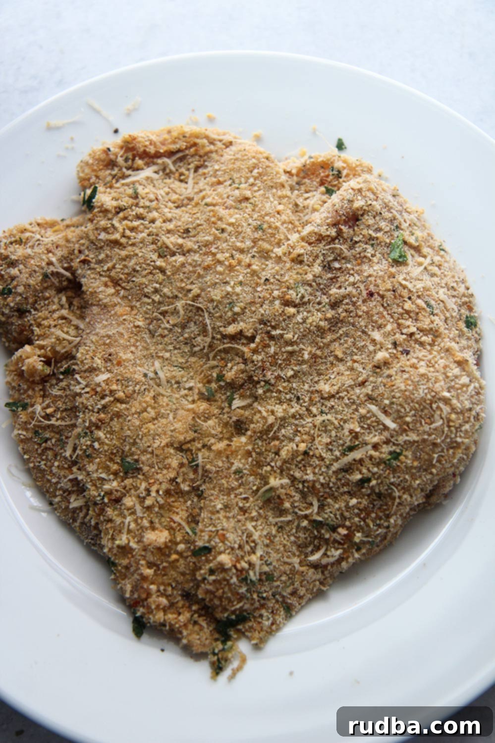 two breaded chicken breasts on a white plate.