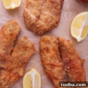 Crispy Fried Tilapia 4 Three golden-brown fried tilapia fillets resting on brown parchment paper.