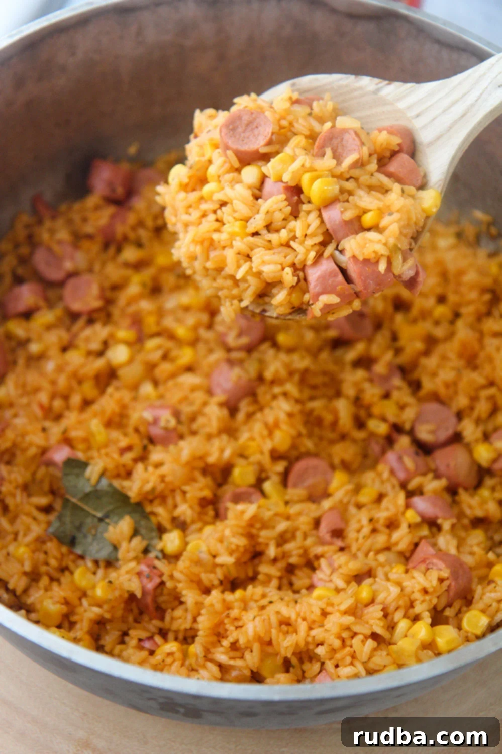 A wooden spoon filled with vibrant yellow Arroz con Salchichas, garnished with fresh cilantro.
