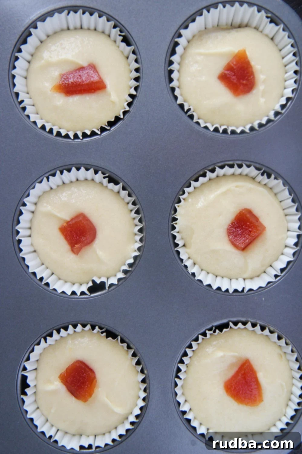 six cupcake liners filled with cupcake batter and guava paste.