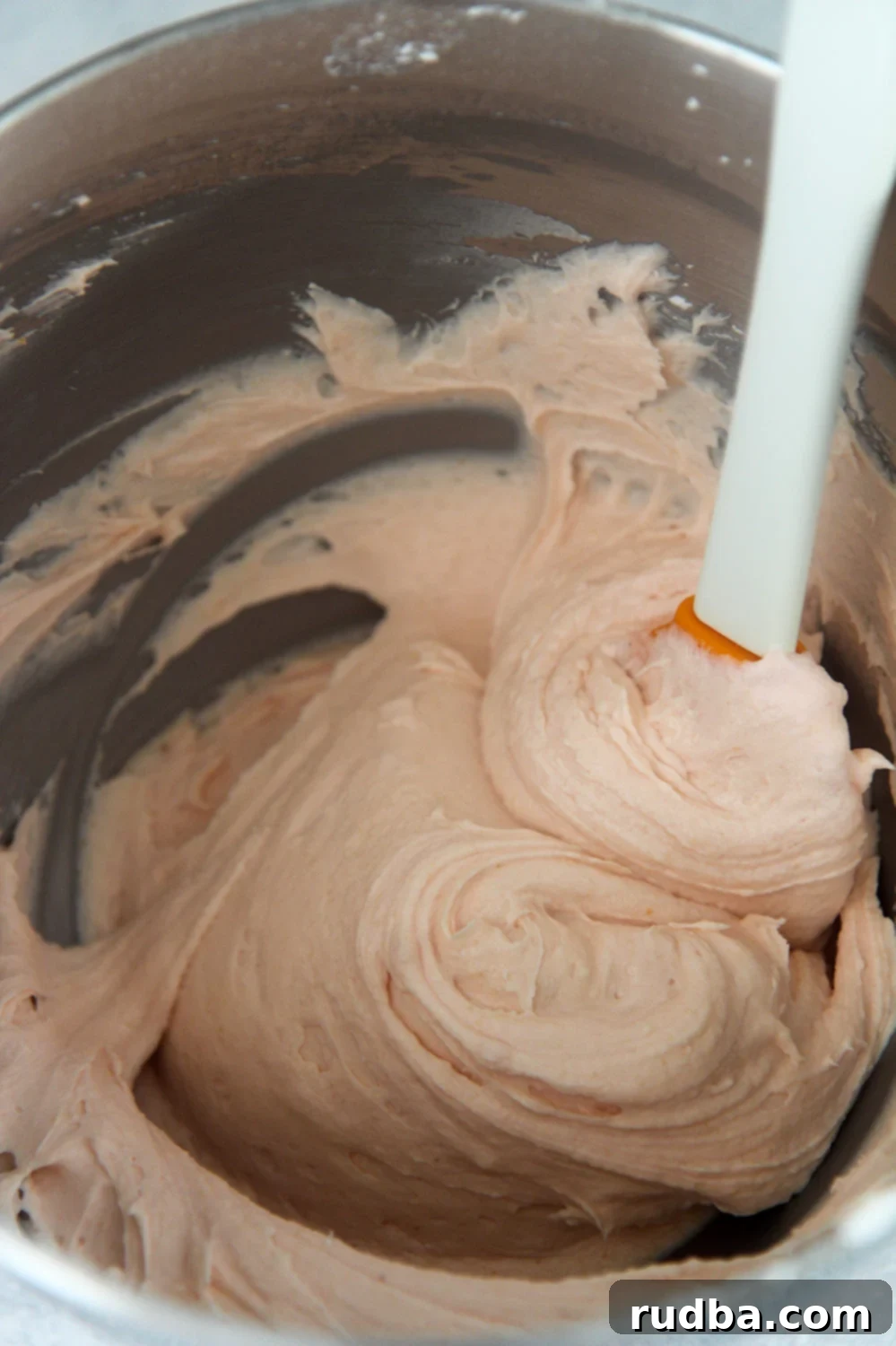 pink cream cheese frosting in a bowl with a spatula.