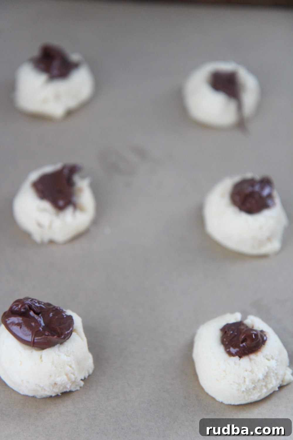 Six cookie balls with Nutella on top, ready for baking.