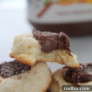 Creamy Nutella Dream Cookies 3 Three Nutella cookies with powdered sugar on top and a Nutella jar in the background.