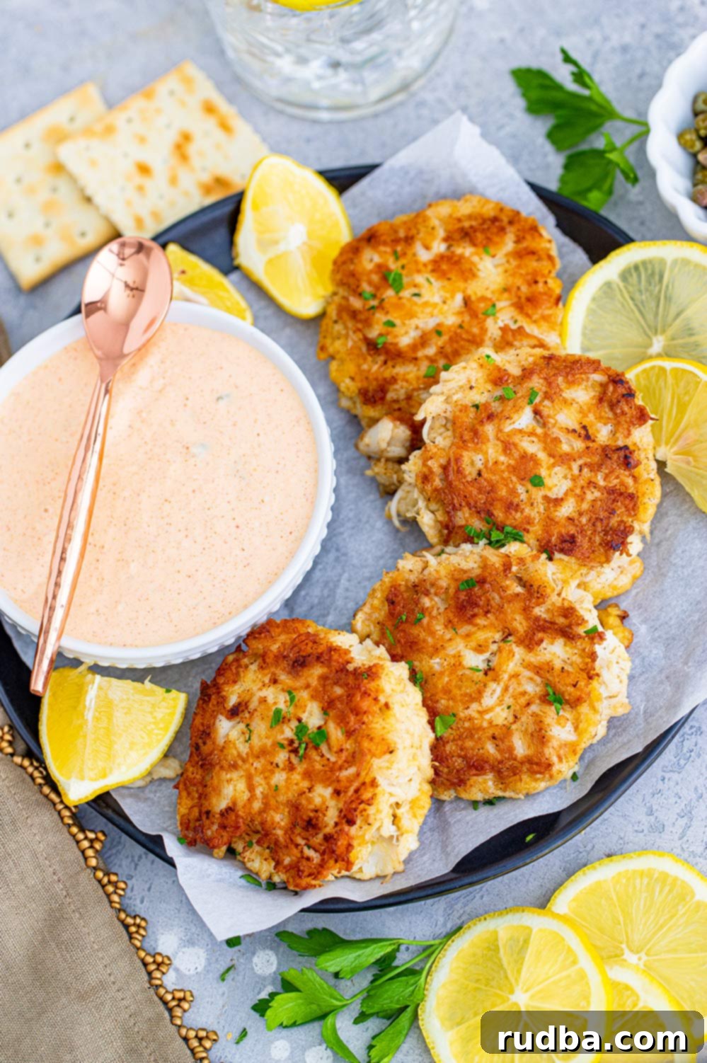 Golden Crab Cakes with Zesty Remoulade 2 four crab cakes on a plate with a side of remoulade sauce and lemon wedges.