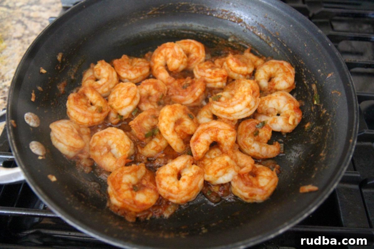 shrimp cooking in a black skillet on a stove top. 
