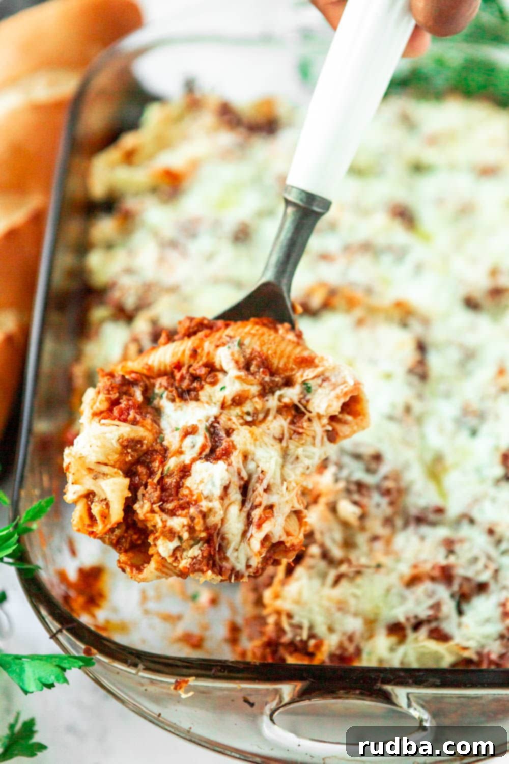 stuffed pasta shells in a 9x13 baking dish with a spoon lifting 3 stuffed shells out of the baking dish. 