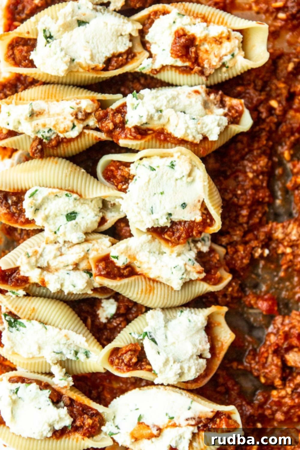 twelve shells filled with ricotta cheese on top of meat sauce 