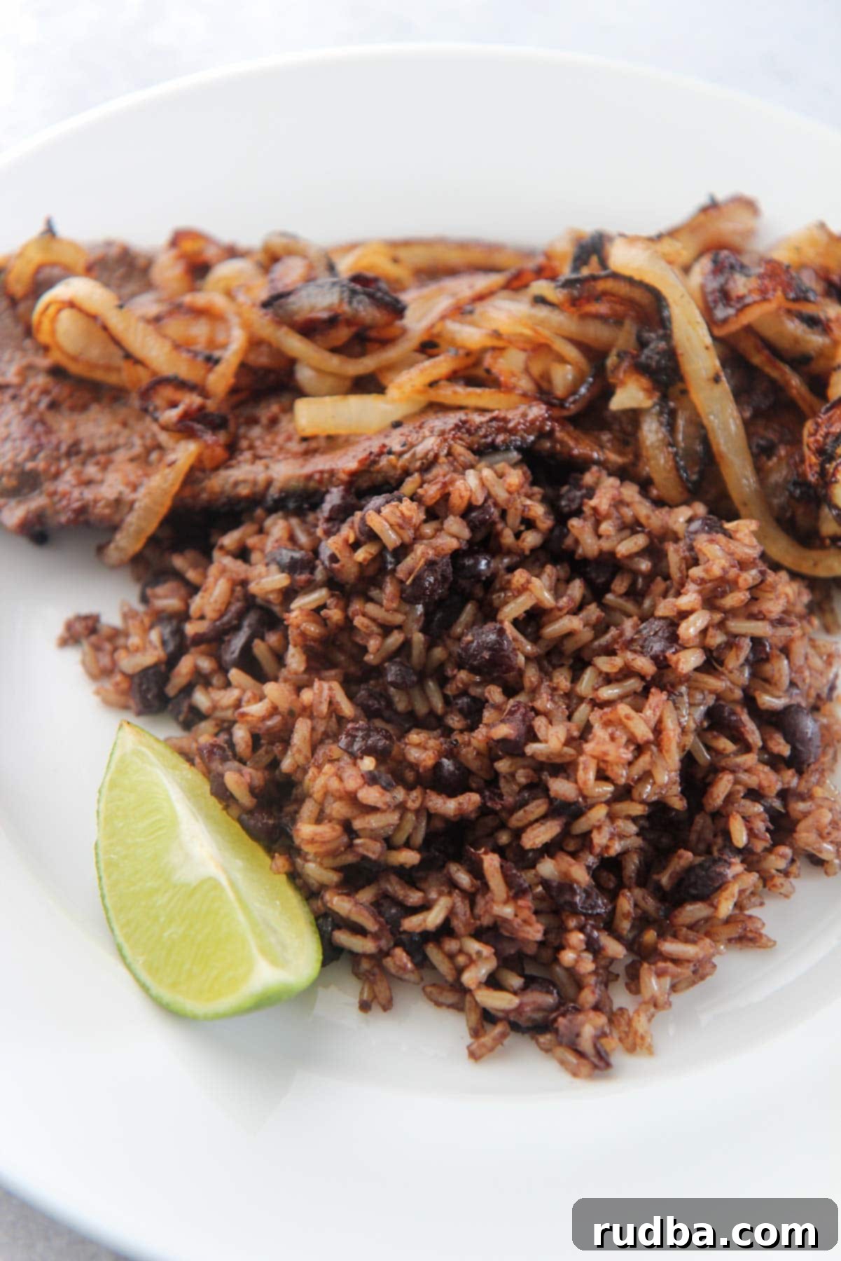 Classic Cuban Black Beans and Rice 1 congri with steak, onions, and a lime wedge.