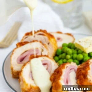 Golden-Crusted Ham & Cheese Chicken 6 chicken cordon bleu on a plate with sauce on top and green peas on the side.
