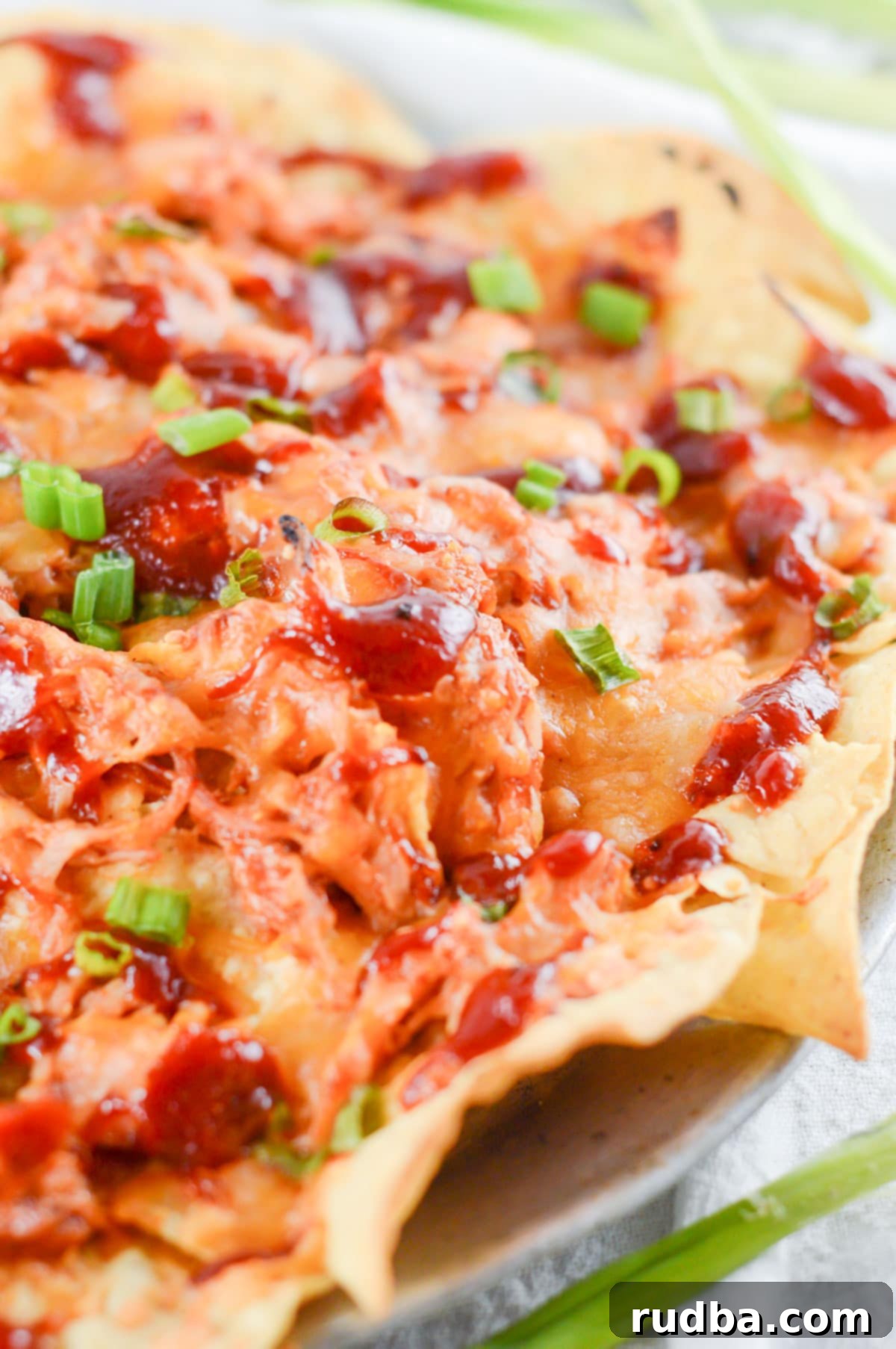 nachos with pulled chicken, bbq sauce, cheese, and scallions on a plate.