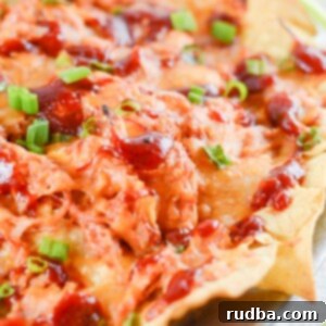 nachos with pulled chicken, bbq sauce, cheese, and scallions on a plate.