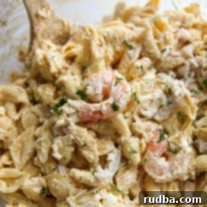 Summer Seafood Pasta Salad 2 seafood pasta salad in a glass bowl with a wooden spoon.